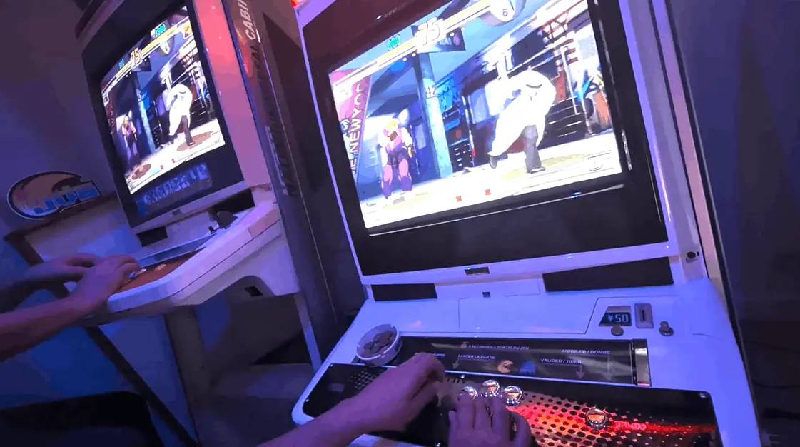 Two arcade cabinets side by side, a fighting game on both screens